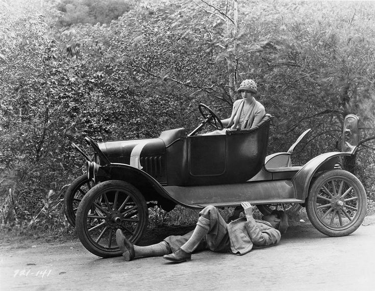 an old photo of a man laying on the ground next to a car