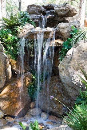 a small waterfall in the middle of some rocks and plants with water coming from it