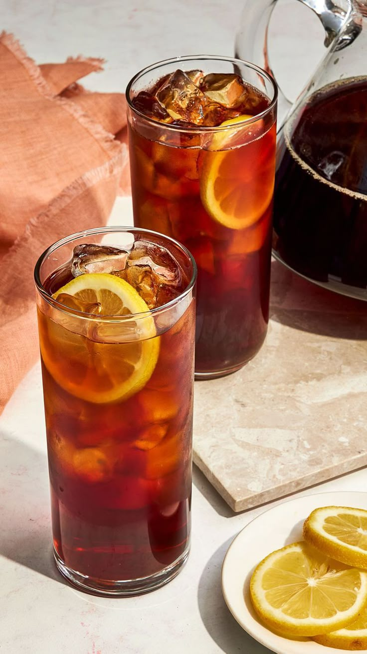 two glasses filled with iced tea and lemon slices on a table next to a pitcher