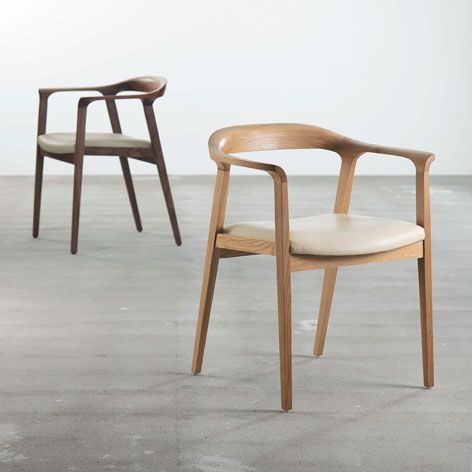 two wooden chairs sitting next to each other on top of a cement floor in front of a white wall