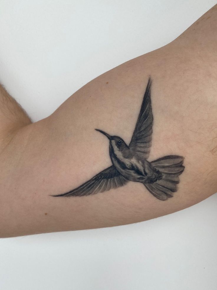 a small tattoo on the arm of a man with a hummingbird flying above it