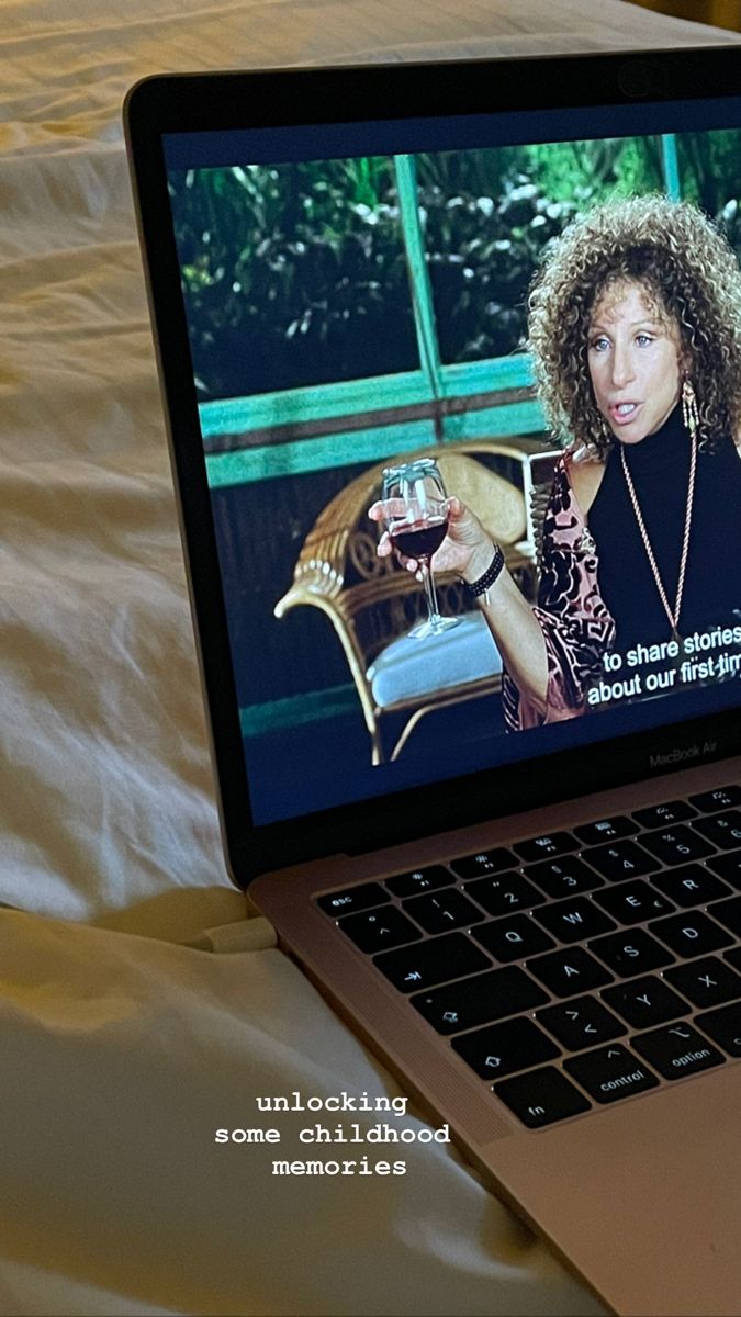 an open laptop computer sitting on top of a bed next to a glass of wine