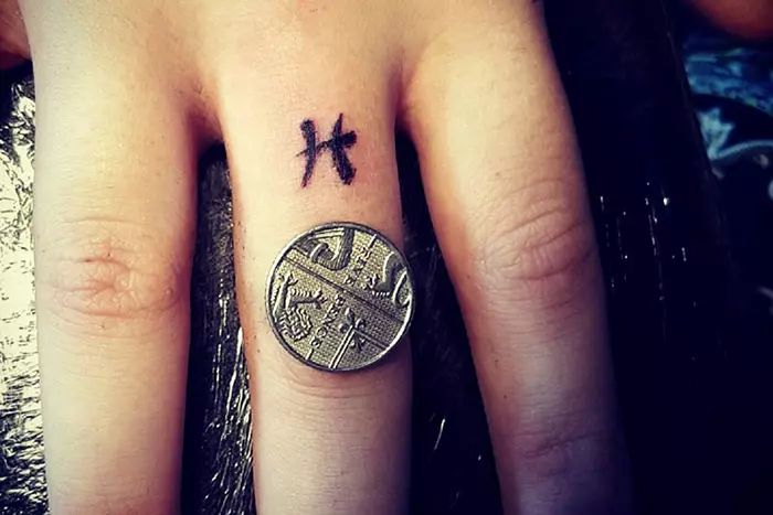 a person with a small cross tattoo on their left hand and a coin in the middle