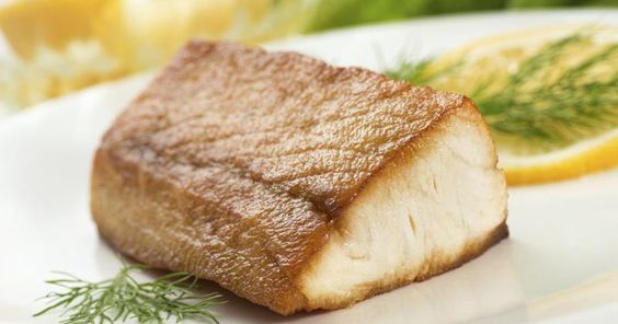 a piece of fish on a white plate with lemon wedges and dill sprigs