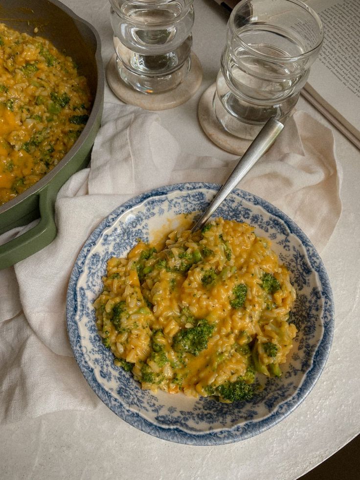 a bowl of broccoli and cheese next to a pan of water on a table