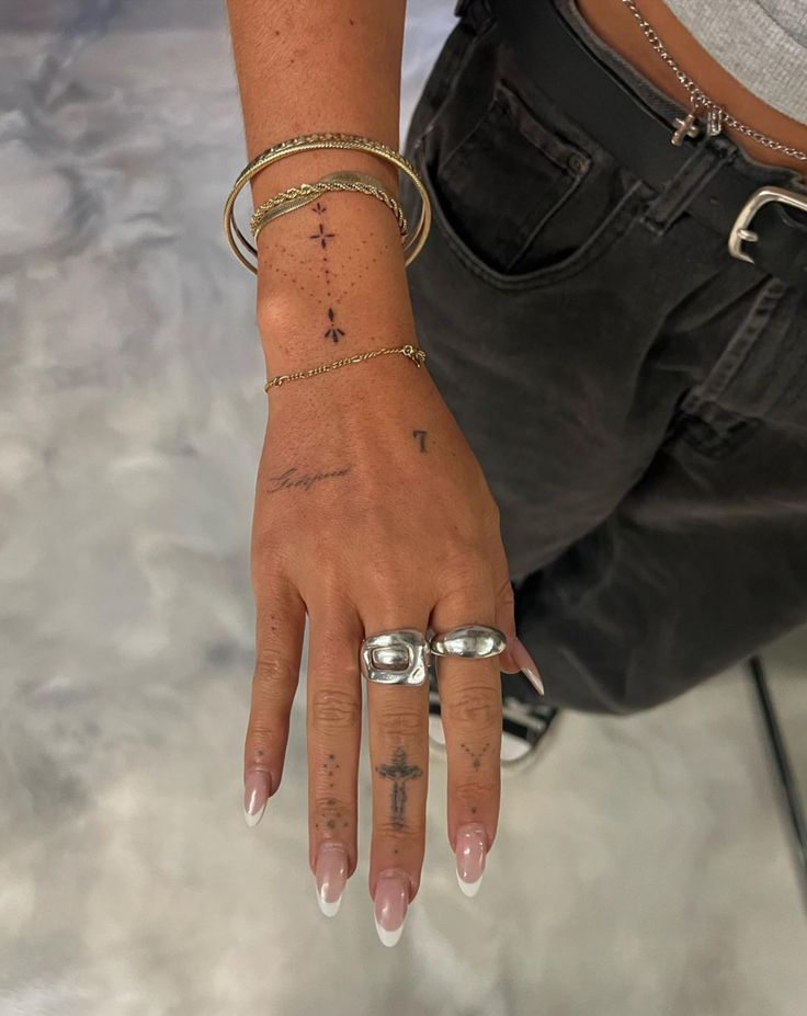 a woman's hand with tattoos on her left wrist and cross tattoo on the middle finger