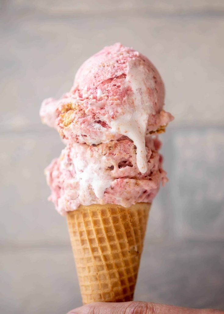 a hand holding an ice cream cone with pink and white topping