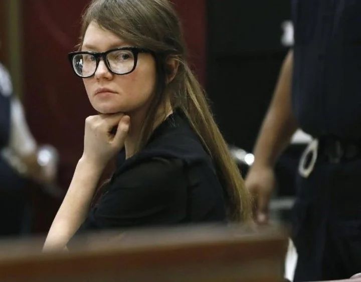 a woman with glasses sitting at a table in front of other people and looking off to the side