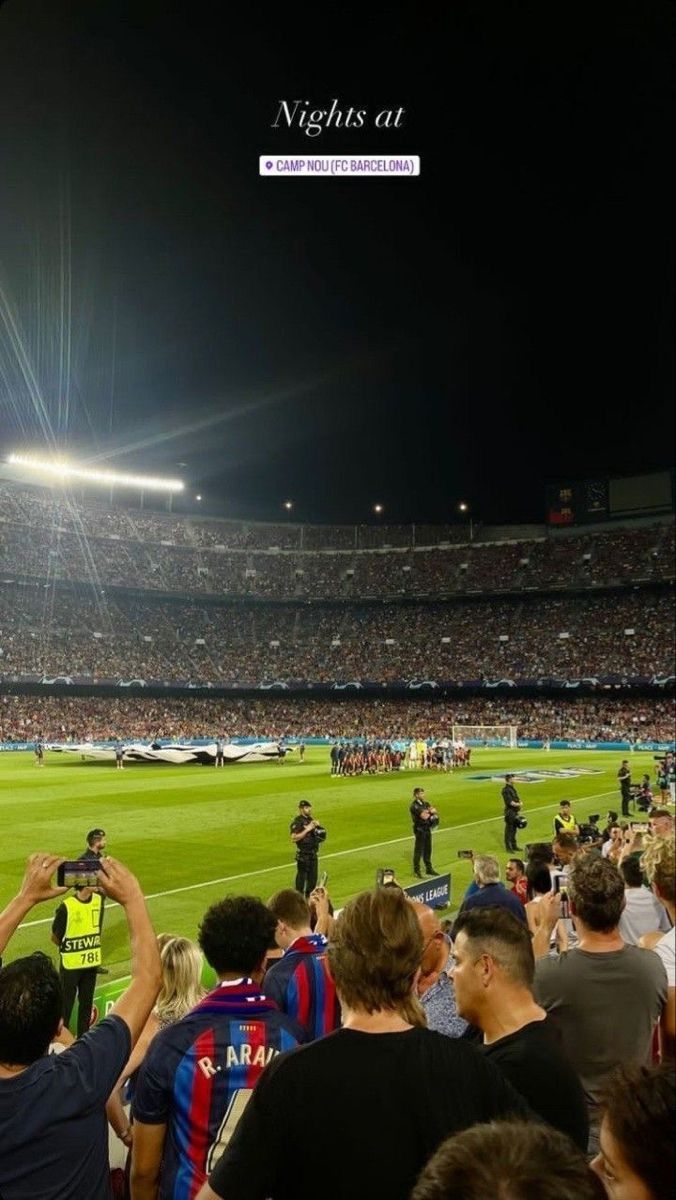 a stadium filled with lots of people standing on top of a soccer field at night