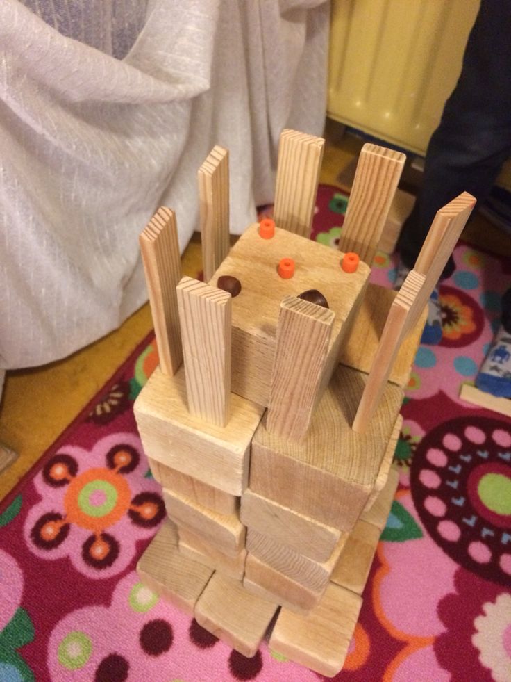 a wooden toy castle made out of wood blocks on a colorful rug in front of a white curtain