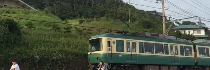 a green and yellow train traveling down tracks next to a lush green hillside