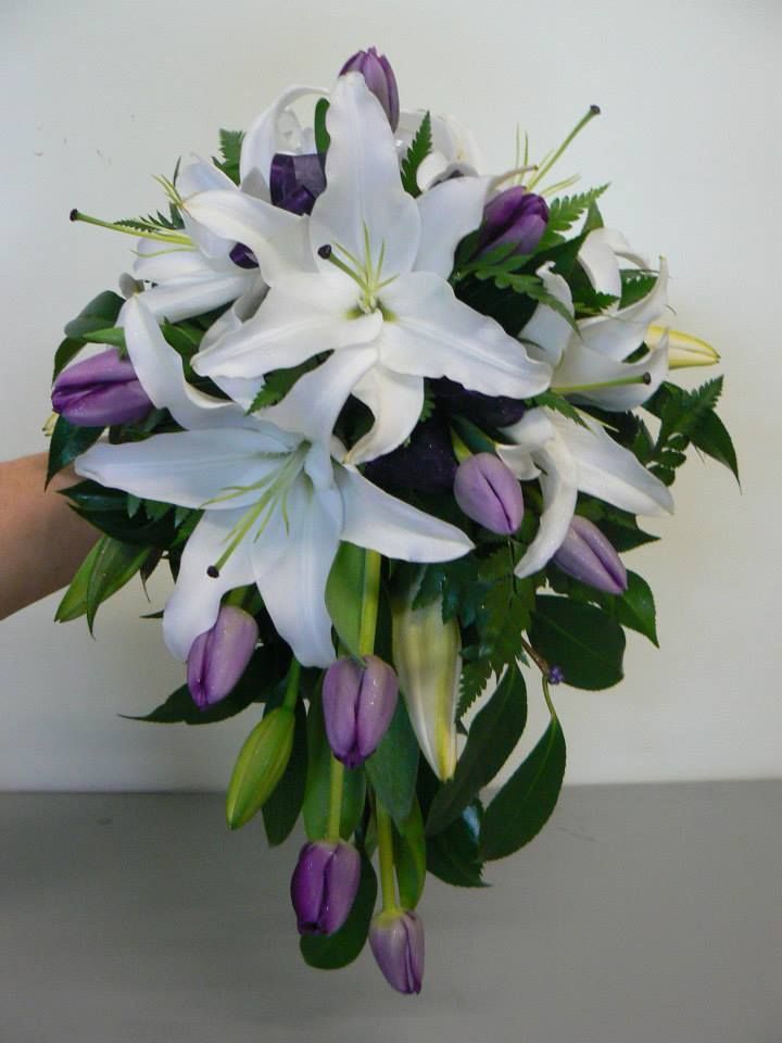 a bouquet of white lilies and purple tulips in someone's hand