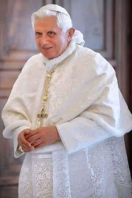 a man in a priest's outfit standing with his hands folded and smiling at the camera