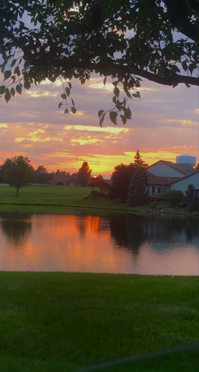 the sun is setting over a small lake in front of a large house and golf course