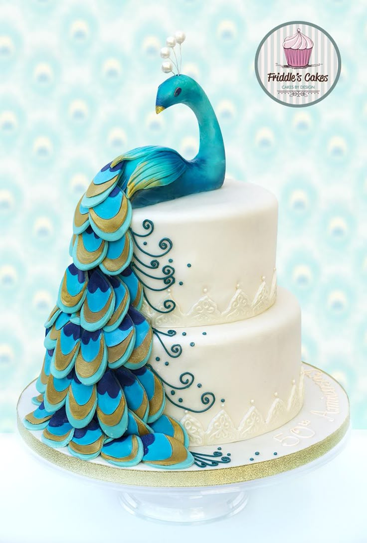 the cake is decorated with blue and gold feathers on it's tiered stand