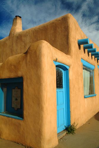 an adobe style building with blue doors and shutters on the outside, against a partly cloudy sky