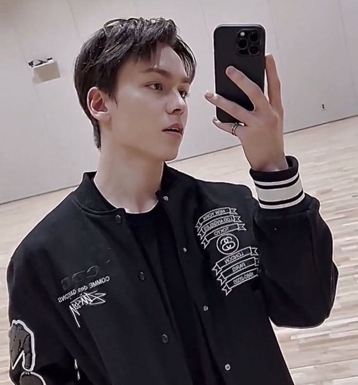 a young man taking a selfie with his cell phone while wearing a black jacket