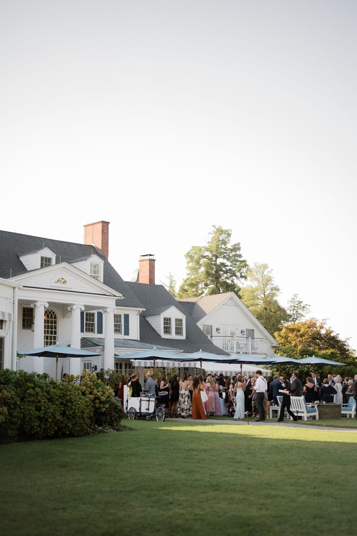 a group of people standing in front of a large white house with an awning