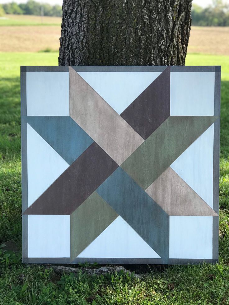 a patchwork quilt hanging on the side of a tree in front of a field