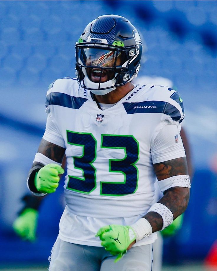 a football player wearing green gloves and holding his hands out to the sidelines with one hand on his hip