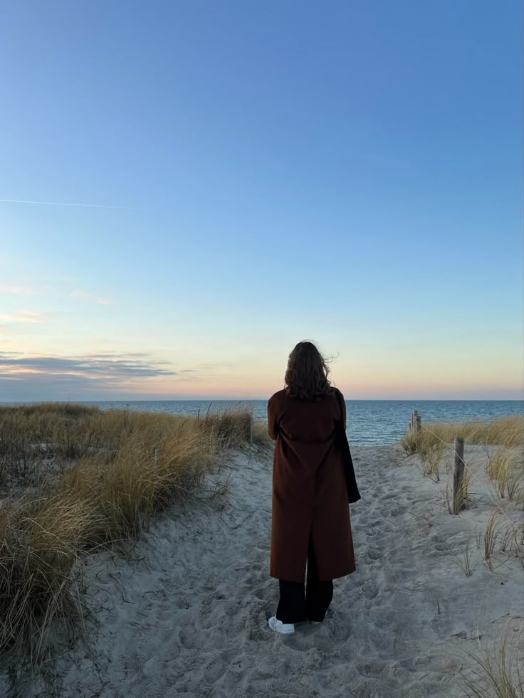 a woman standing on top of a sandy beach next to the ocean in front of a blue sky