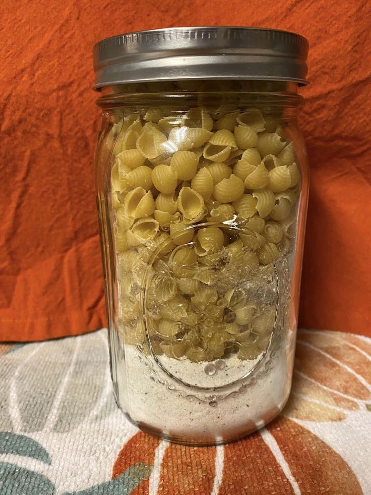 a jar filled with macaroni and cheese sitting on top of a table cloth