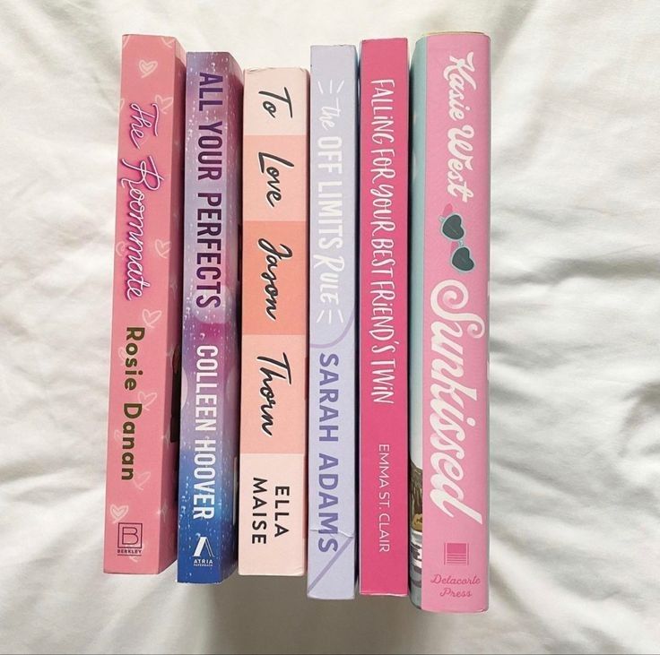 a stack of books sitting on top of a white bed covered in pink and blue covers