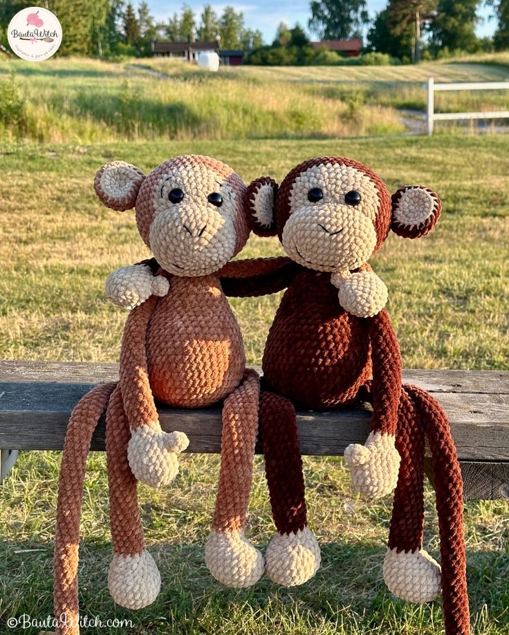 two crocheted monkeys sitting on top of a wooden bench in the grass next to each other