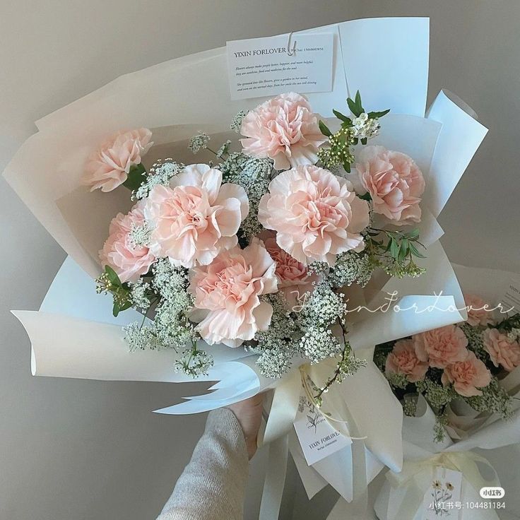 a bouquet of pink carnations and baby's breath wrapped in white paper