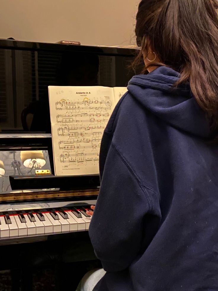 a person sitting in front of a piano with sheet music on the keyboard behind them