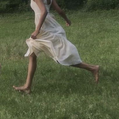 a woman in a white dress playing frisbee with a dog on the grass