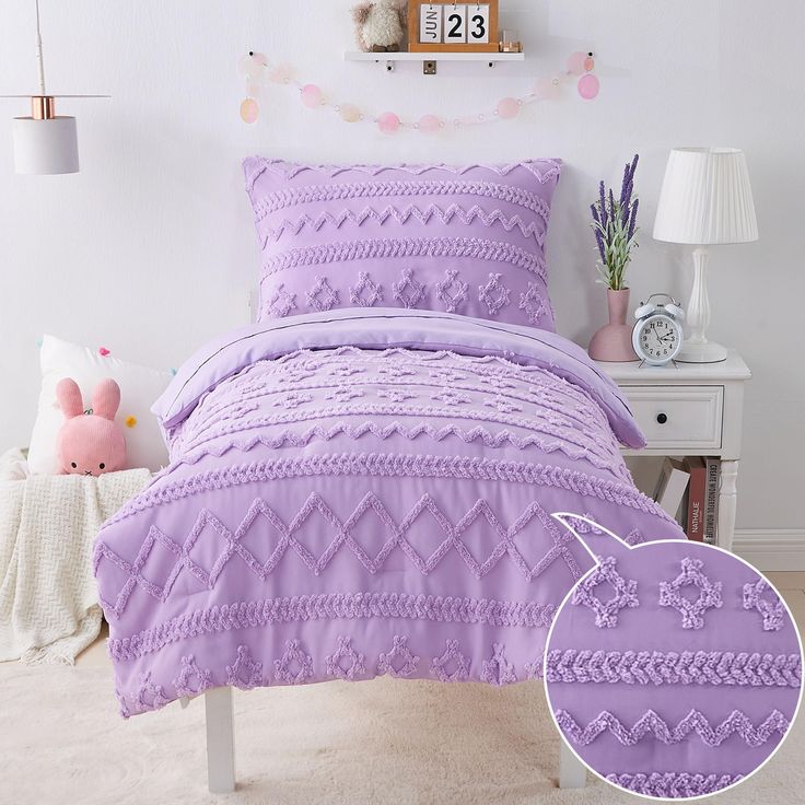 a bed with purple comforter and pillows in a room next to a white nightstand