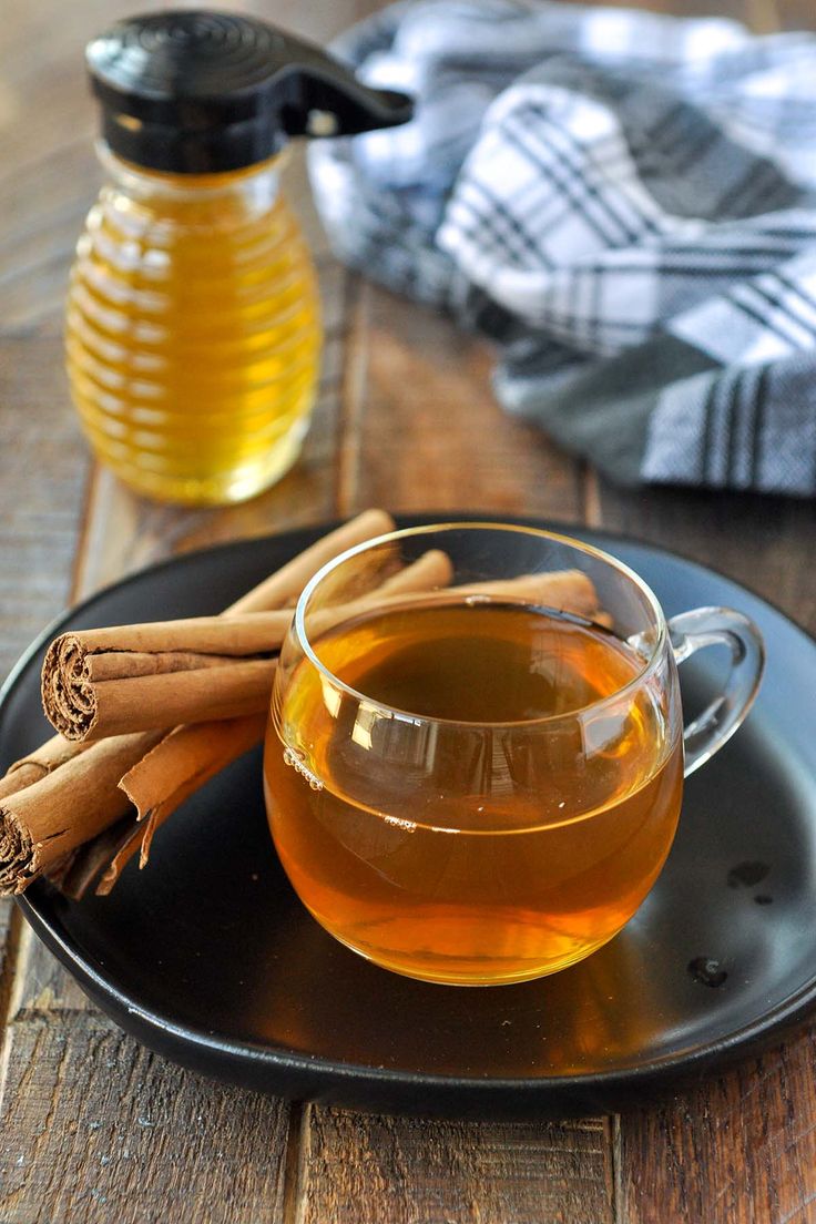 a cup of tea with cinnamon sticks on a plate next to a jar of honey