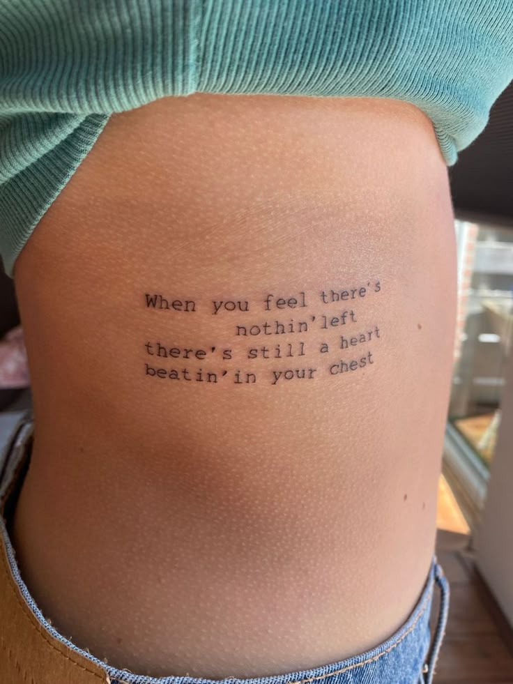 the back of a woman's stomach with a tattoo saying, when you feel there's nothing left there's still a heart beating in your gut