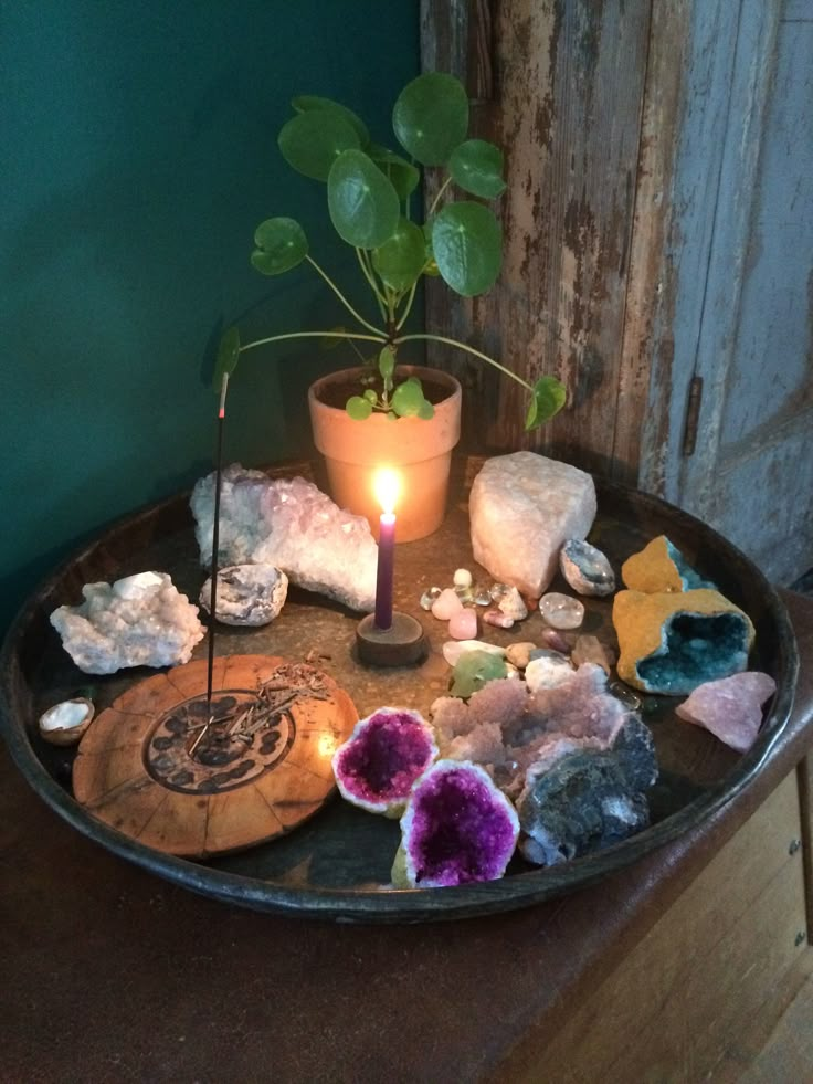 a tray with rocks and a candle on top of it next to a potted plant