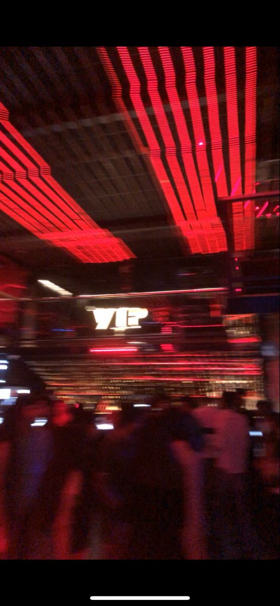 blurry photograph of people in a bar with red lights on the ceiling and overhead lighting