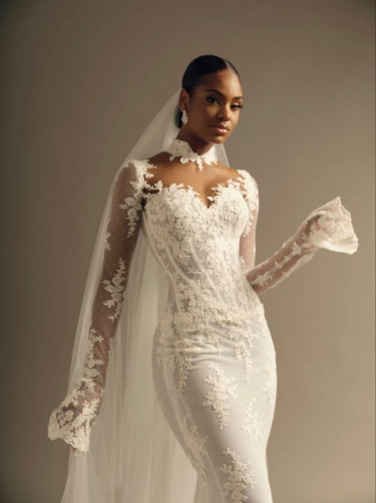 a woman in a white wedding gown and veil posing for the camera with her hands on her hips