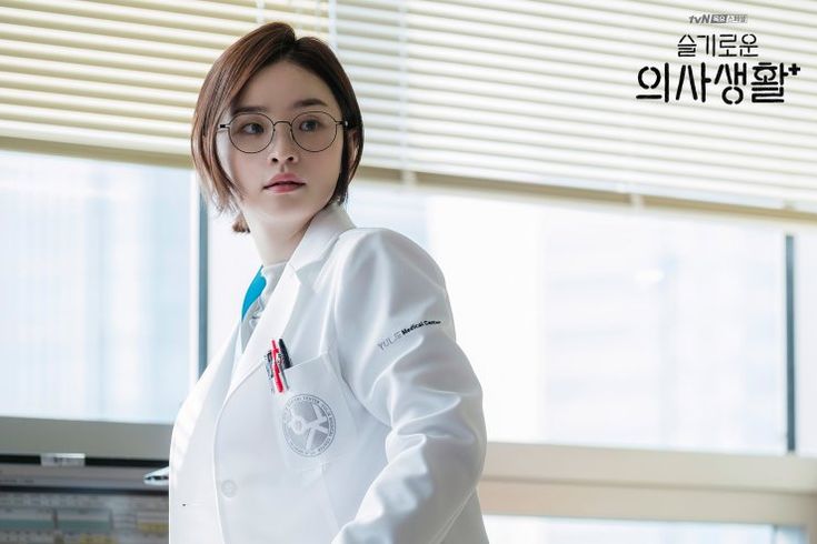 a woman in white lab coat standing next to a window