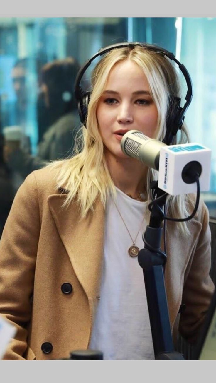 a blonde woman with headphones on is talking into a microphone and looking at the camera