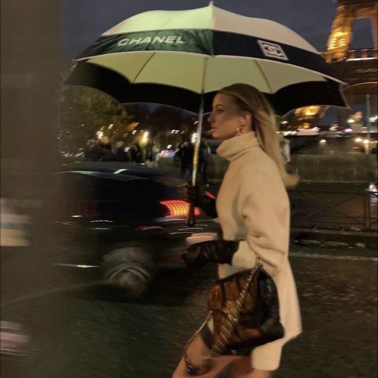 a woman walking down the street with an umbrella over her head, in front of the eiffel tower at night