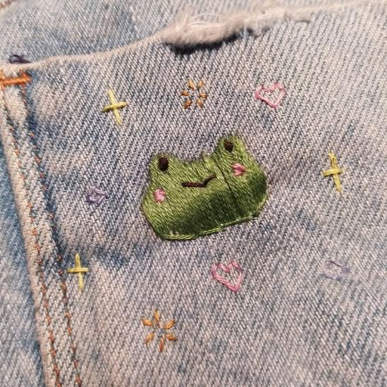 a close up of a pair of jeans with embroidered frog on it's pocket