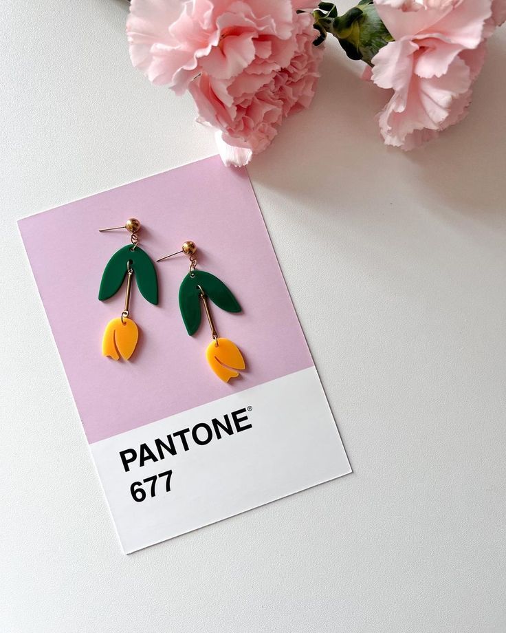 a pair of yellow and green earrings sitting on top of a card next to pink flowers