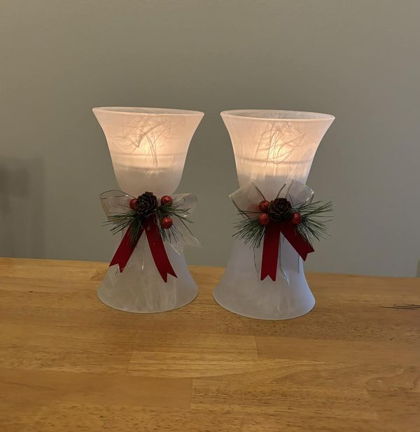 two white vases with red bows and pine cones on them sitting on a table