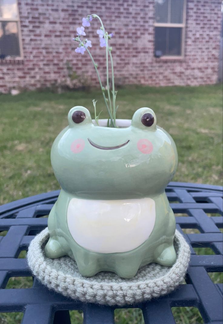 a green frog sitting on top of a blue table next to a purple flower pot