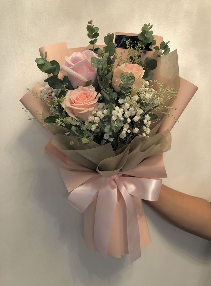 a bouquet of pink roses and baby's breath is wrapped in brown paper with greenery