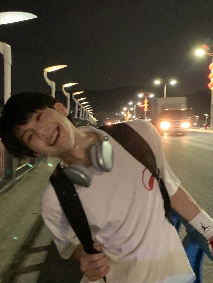 a man with headphones on standing next to a bike and street lights at night