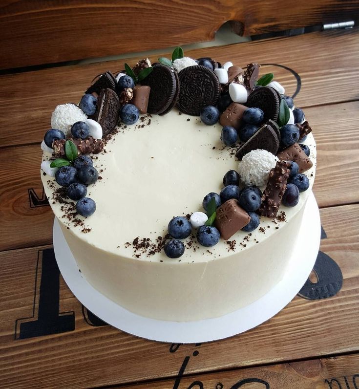 a white cake with blueberries and oreo cookies on top is sitting on a wooden table