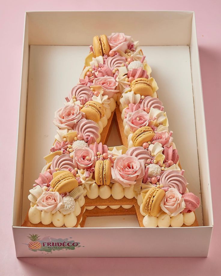 a cake shaped like the letter e in a box with flowers and macaroons