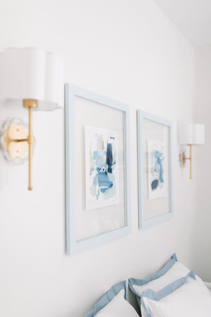 two framed pictures hang on the wall above a bed with blue and white pillows in a bedroom