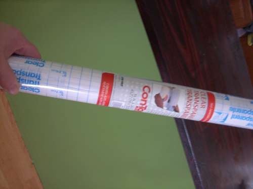 a person holding a tube of toothpaste on top of a wooden table next to a green wall